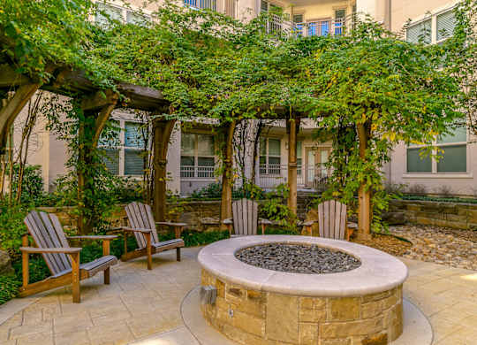 a fire pit with two chairs and a pergola in front of a building