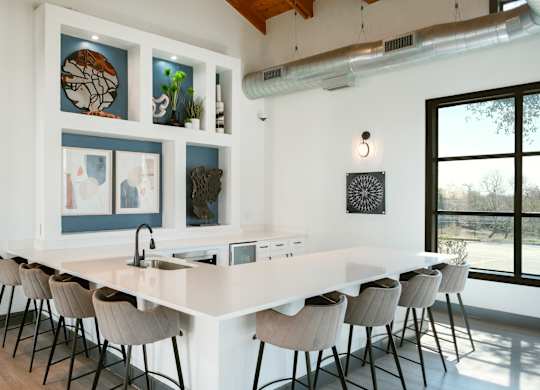 A kitchen with a long white island and chairs.