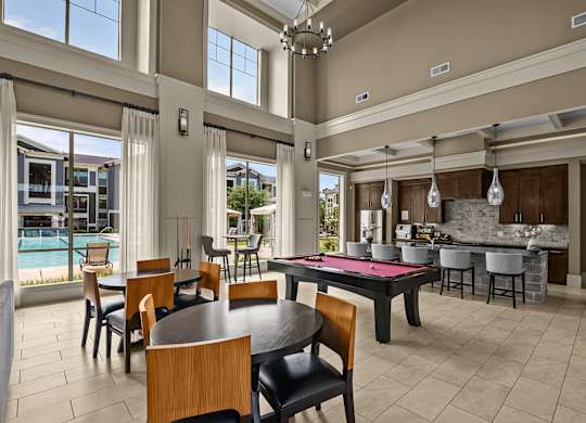 A modern dining room with a pool table and a kitchen in the background.