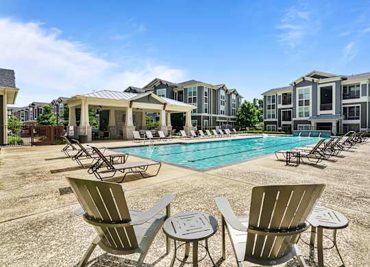 A pool surrounded by chairs and tables in front of apartment buildings.