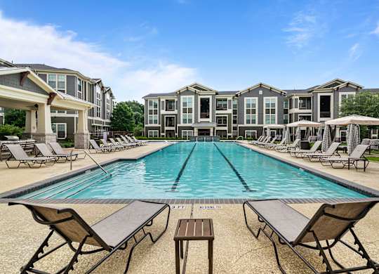 A large swimming pool surrounded by lounge chairs and apartment buildings.