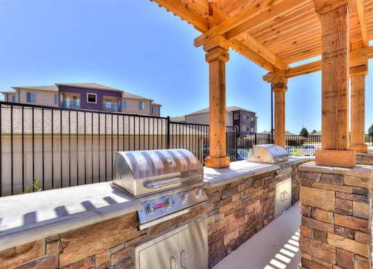 A BBQ grill is on a patio with a stone wall and a wooden pergola.