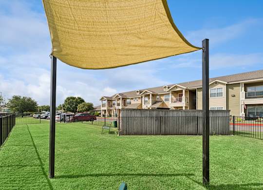 A yellow shade sail over a green lawn in front of apartment buildings.