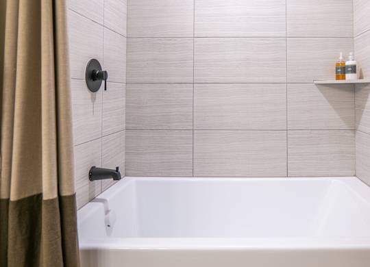 A white bathtub in a bathroom with beige tiles and a beige shower curtain.