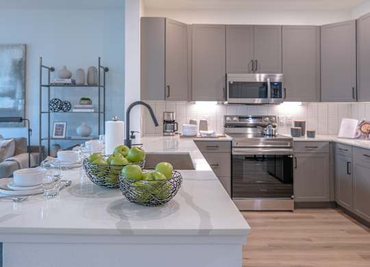 A modern kitchen with a white island and a bowl of green apples on it.