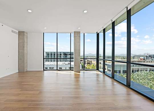 A large empty room with wooden floors and a view of the city through large windows.