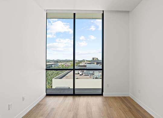 A room with a sliding door that opens to a balcony with a view of the city.