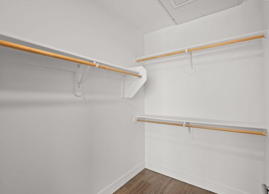 A white closet with two shelves and a wooden floor.