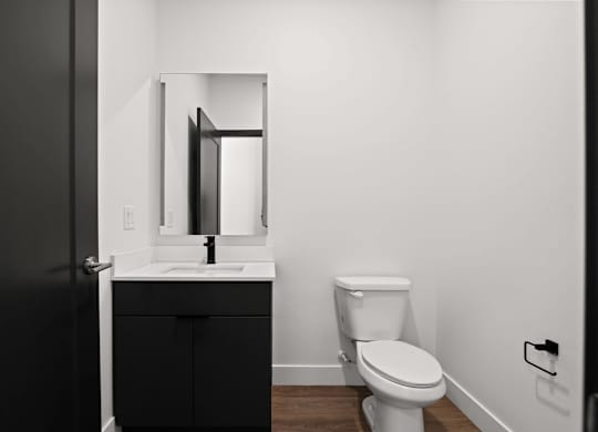 A black door is open to a white bathroom with a toilet and sink.