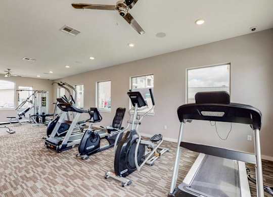 A home gym with a treadmill, elliptical machines, and a fan.