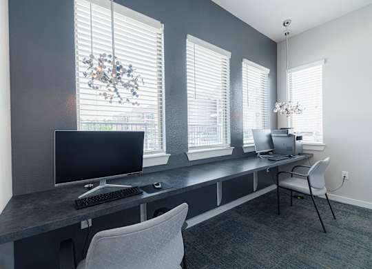 A modern home office with a black computer monitor and keyboard on a desk with a chair.