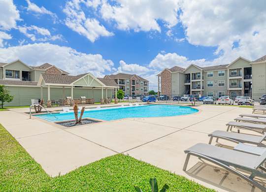 A swimming pool surrounded by lounge chairs in a residential area.