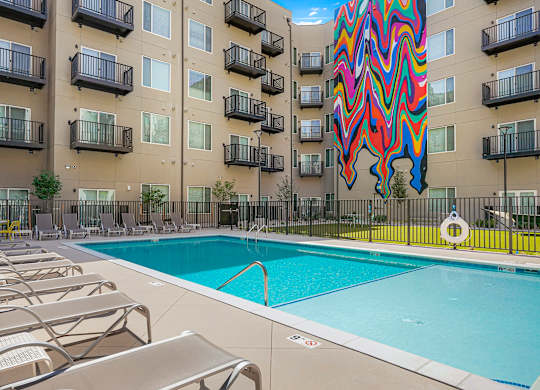 A large pool with lounge chairs in front of apartment buildings.