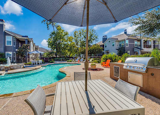 A pool area with a table and chairs under an umbrella.