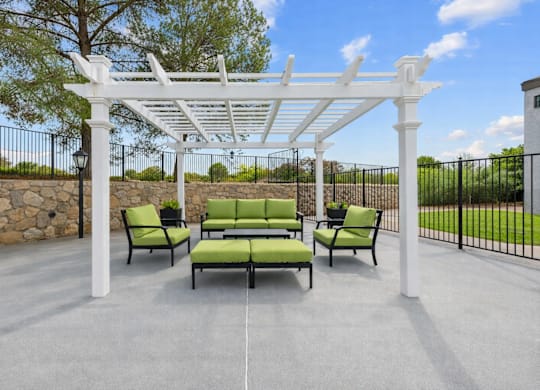 A white pergola with green cushioned seating is in the foreground of a patio.