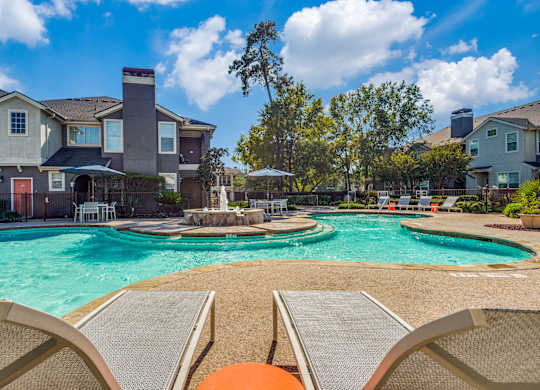 A swimming pool surrounded by lounge chairs and a row of houses in the background.