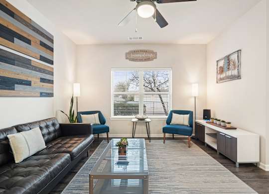 A living room with a black leather couch, a glass coffee table, and a ceiling fan.