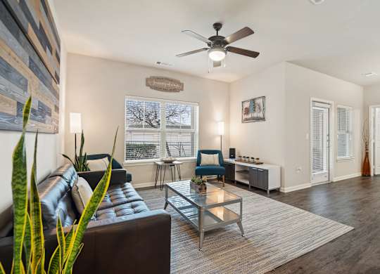 A living room with a brown leather couch, a glass coffee table, and a ceiling fan.