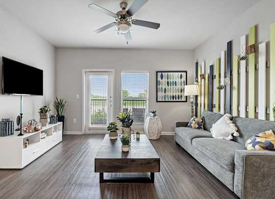 A living room with a grey couch, a wooden coffee table, a flat screen TV, and a ceiling fan.