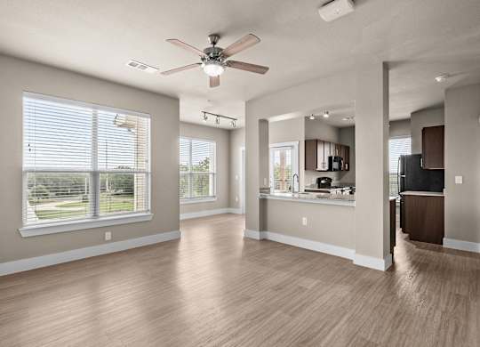 an empty living room with a ceiling fan and a kitchen