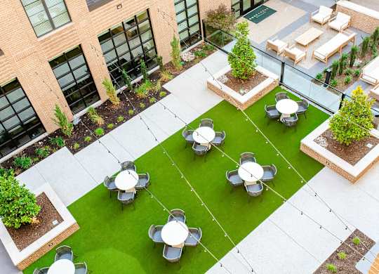 A courtyard with a green lawn and white tables.