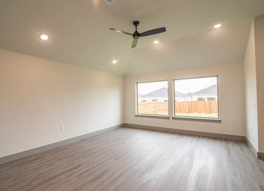Empty room with a ceiling fan and two windows.