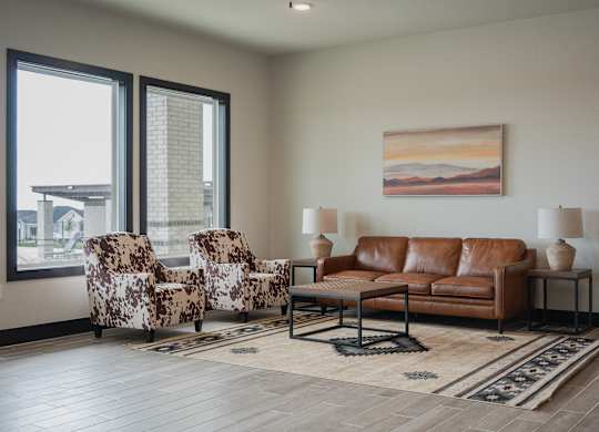 A living room with a brown leather couch, two patterned chairs, and a painting on the wall.