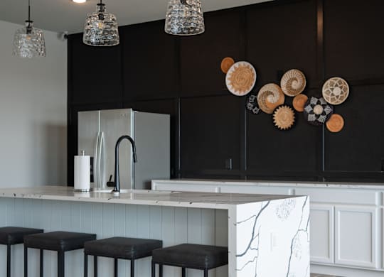 A kitchen with a white marble island and black bar stools.