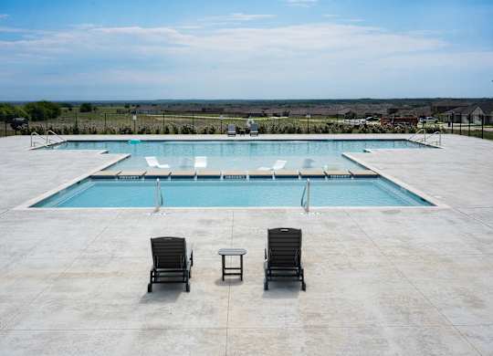 A large swimming pool with two lounge chairs and a table.