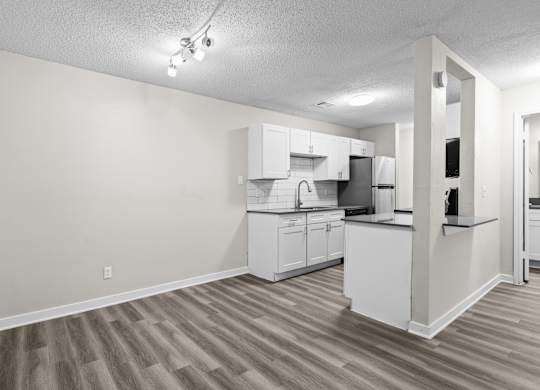 the living room and kitchen of an apartment with a wood floor and white cabinets