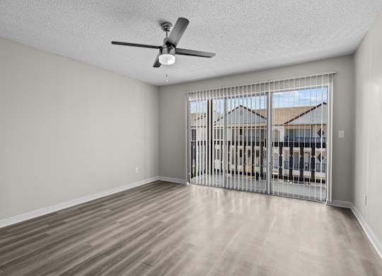 an empty living room with a large window and a ceiling fan