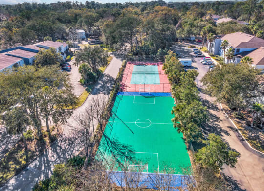 an aerial view of a basketball court and tennis court in a neighborhood with trees