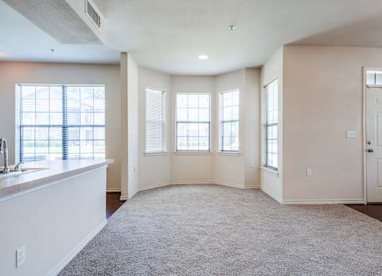 an empty living room with windows and a kitchen