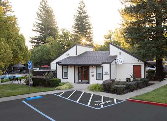 A white building with a clock on the front and a parking lot in front of it.
