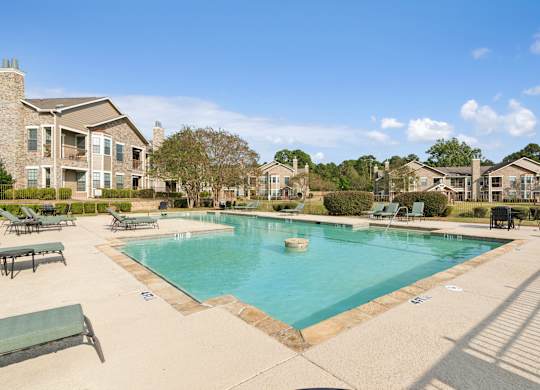 A large swimming pool surrounded by a concrete patio and lounge chairs.