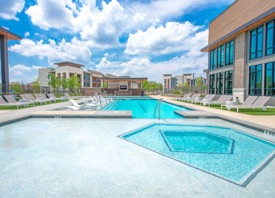 a large swimming pool with lounge chairs and a building in the background