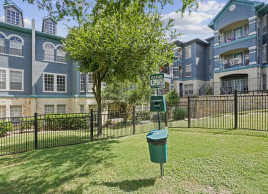A tree in front of a building with a green trash can in front of it.