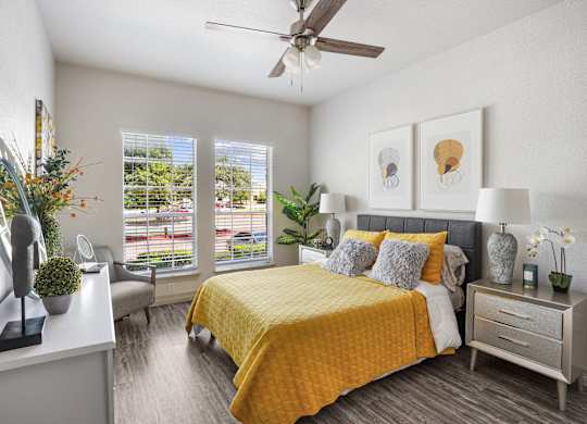 A bedroom with a yellow bedspread and a ceiling fan.