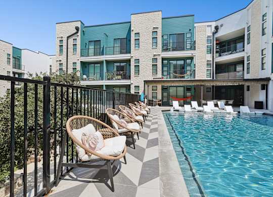 A pool area with chairs and a building in the background.