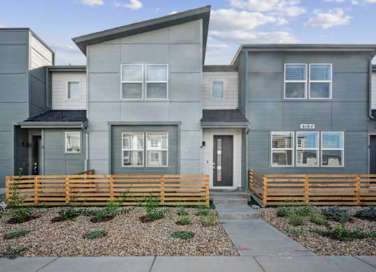 A modern house with a grey facade and a wooden fence in front.