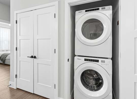 A white washing machine is stacked on top of a white dryer in a white cabinet.