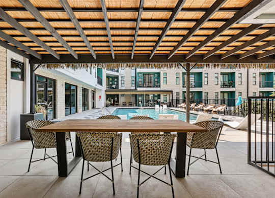 A table with chairs is set up outside with a pool and buildings in the background.