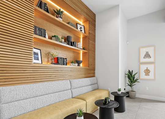 A living room with a yellow couch, a wooden shelf with books and plants, and a painting on the wall.