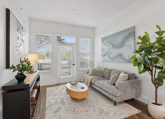 A living room with a grey couch, a coffee table, a potted plant, and a painting on the wall.