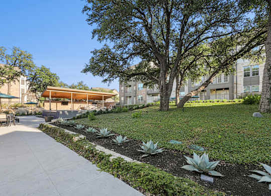 A concrete walkway leads through a landscaped area with a building in the background.