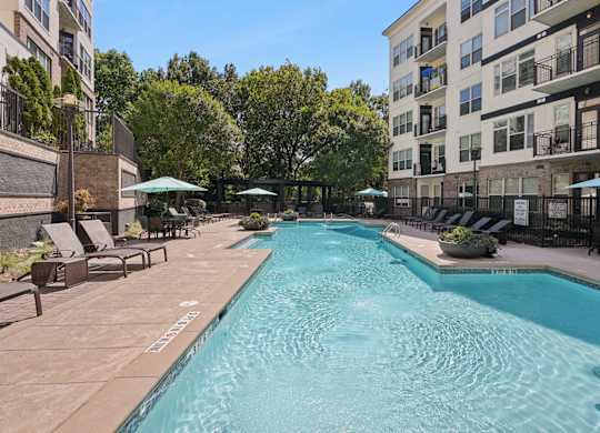 A large swimming pool surrounded by lounge chairs and umbrellas in a residential area.
