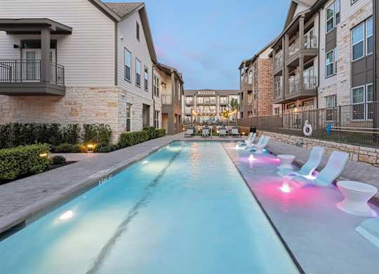 A long rectangular pool with a blue tint is surrounded by white lounge chairs.