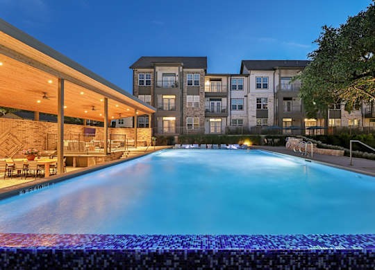 A large swimming pool in front of a building at dusk.