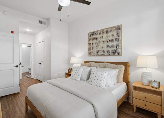 A bedroom with a large bed, a nightstand, and a ceiling fan.