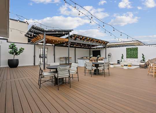 A wooden deck with chairs and tables is surrounded by a white building.